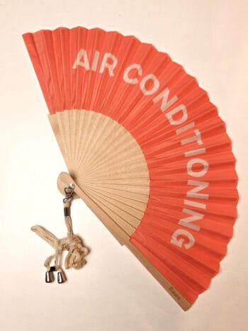 Håndvifte i træ, med teksten AIRCONDITIONING på peach baggrund, fra fisura