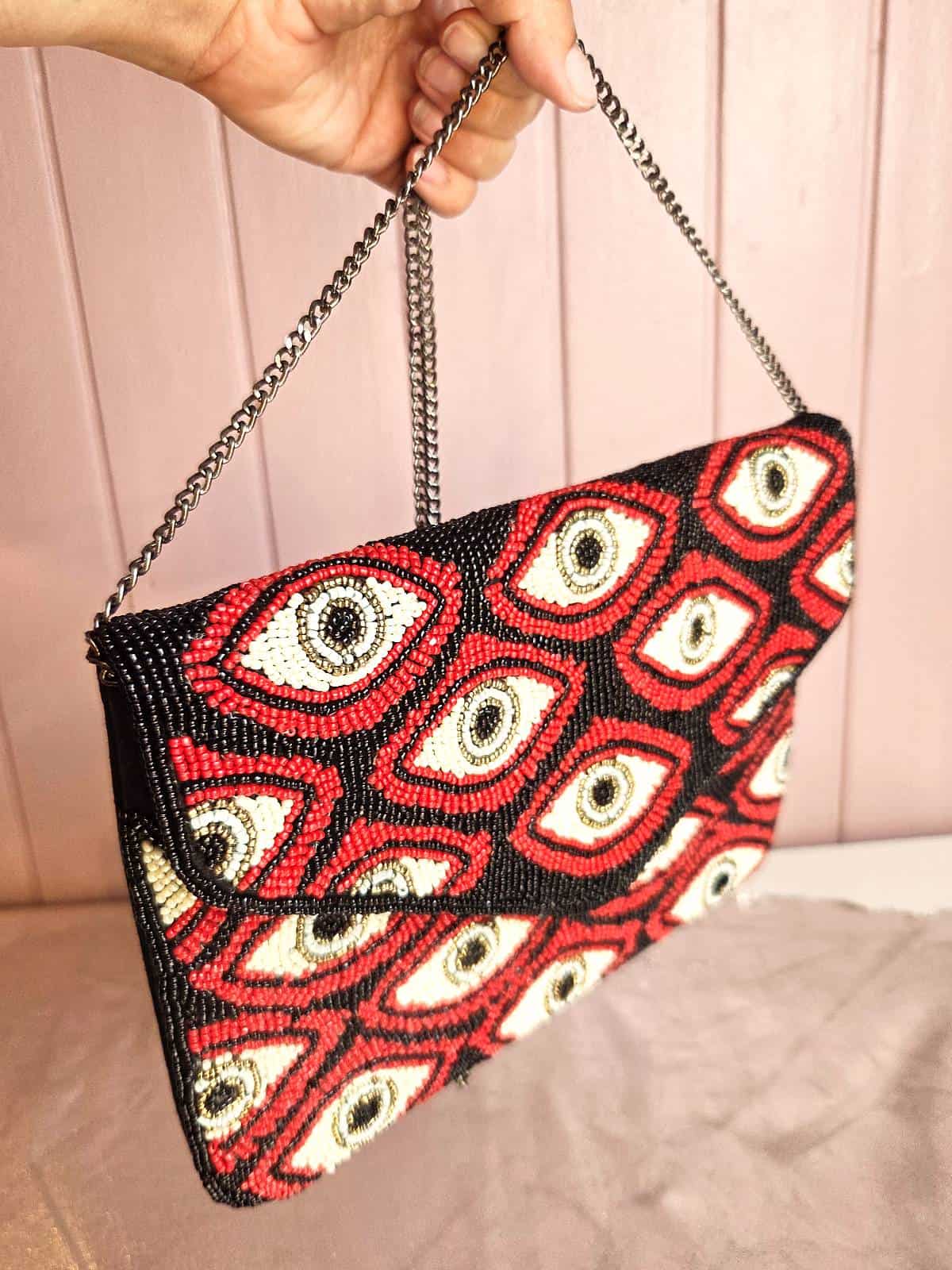 perleclutch med øjne - rød og sort - holdt oppe i hånd