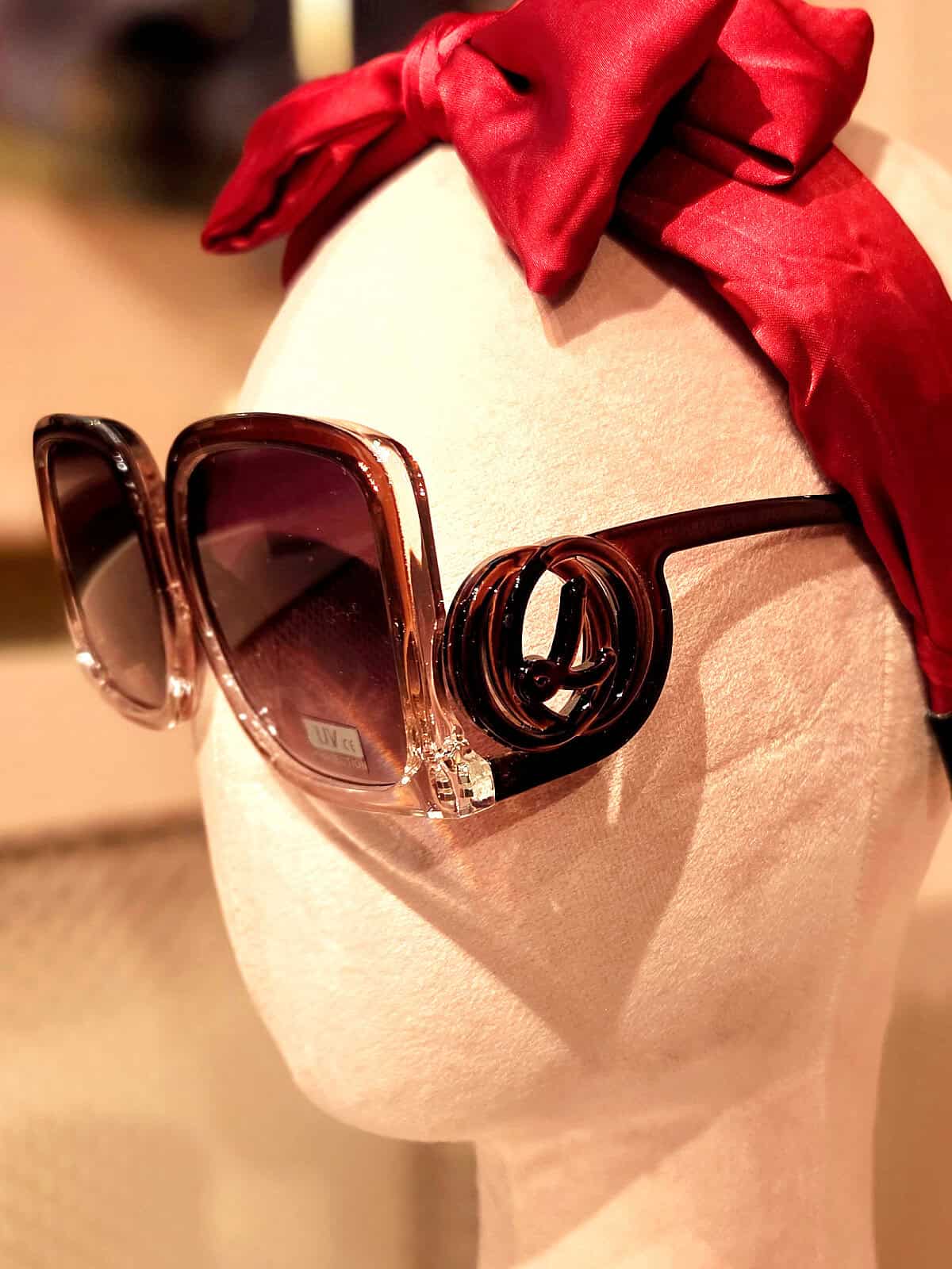 Solbriller med store, mørke linser og rød hårbøjle.