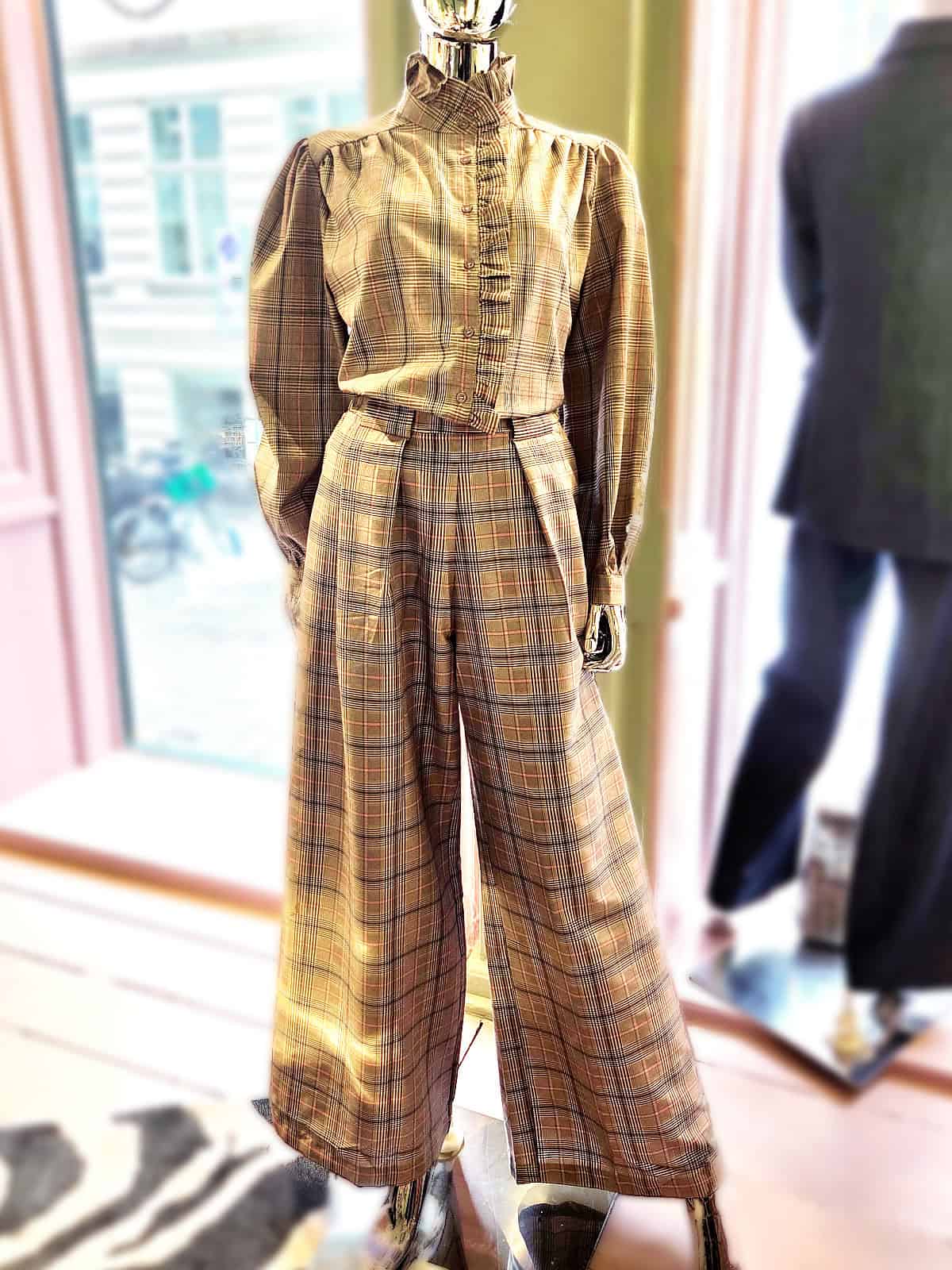 Ternet skjorte med flæser og brede bukser i et butiksmiljø.