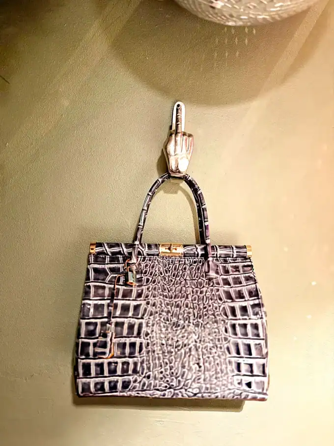 Vægkrog formet som hånd med guldhånd, holder en elegant taske.