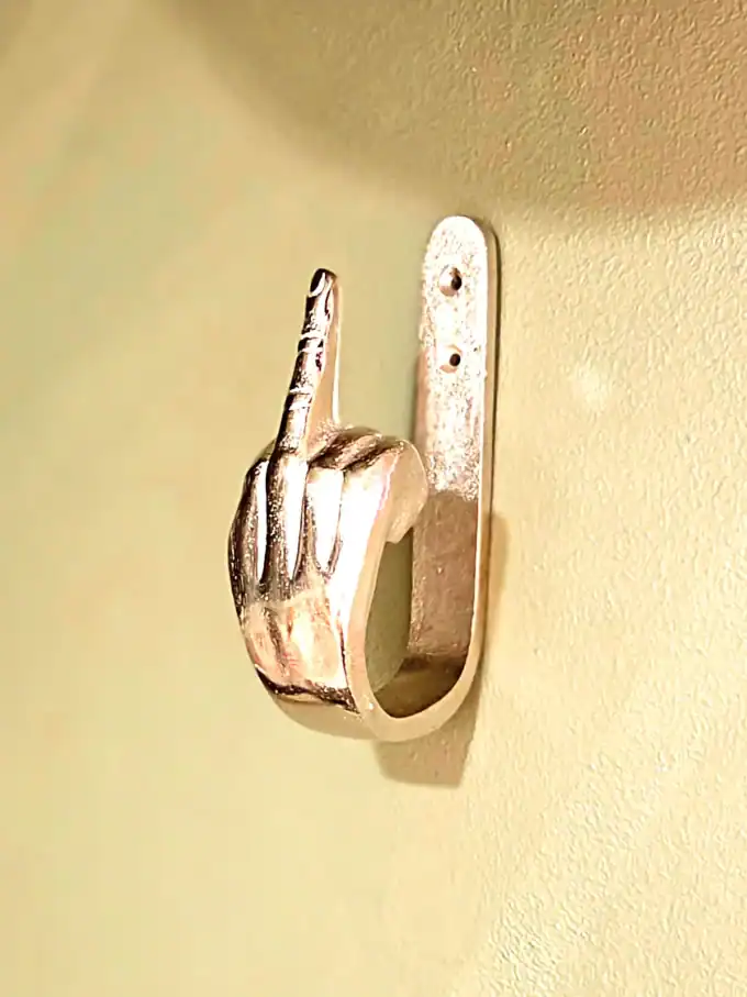 Vægkrog formet som en hånd med midterfingersymbol i guld. Perfekt til moderne hjem og unikke indretn.