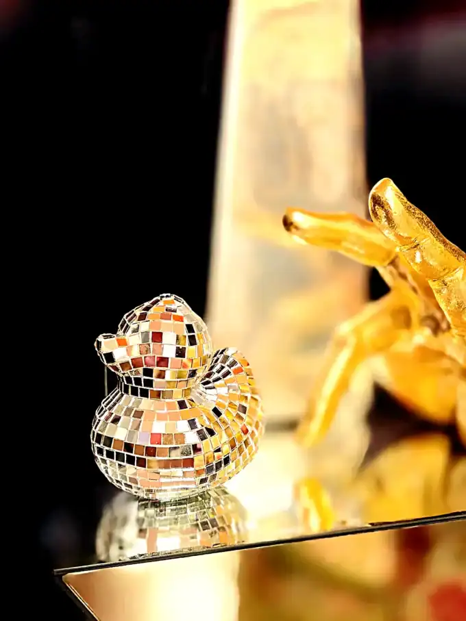 Lille bling-dukke med spejlende mosaikdesign på en sort overflade.