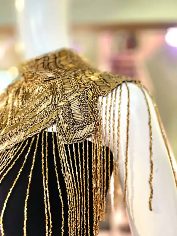 Guld- og perlepyntet capelet med elegante detaljer, perfekt til festlige begivenheder og specielle anl.