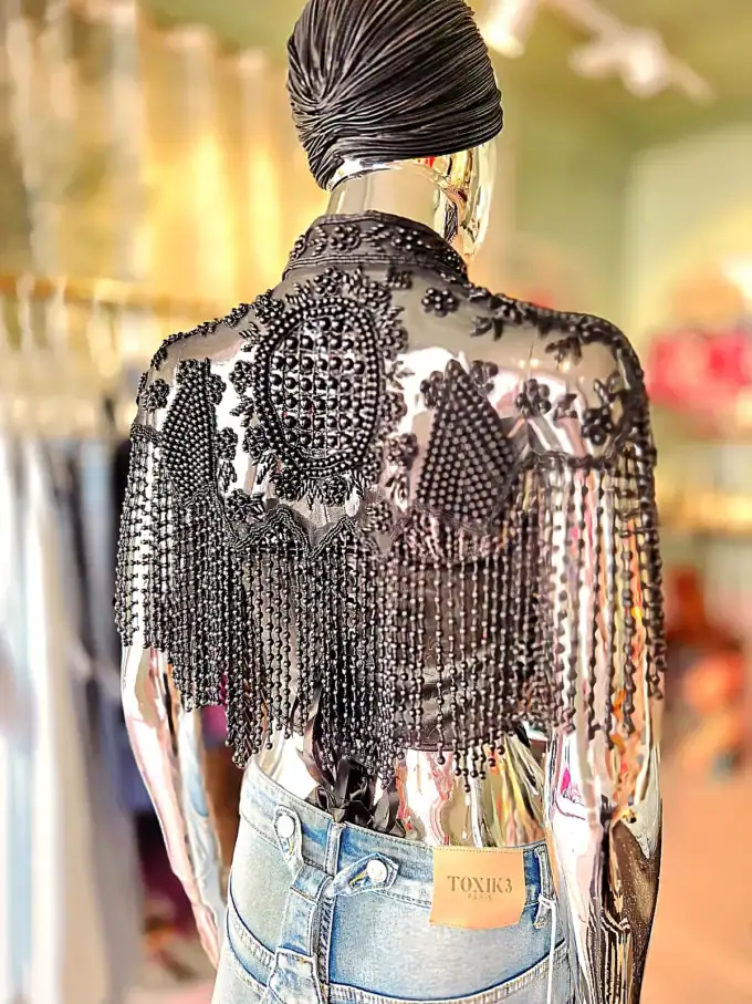 Moderne kvinde i glitrende perlekappe og jeans, set bagfra i butiksmiljø.