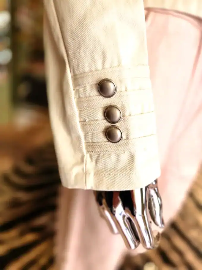 Detalje af denimjakke med metalknapper på ærmet.