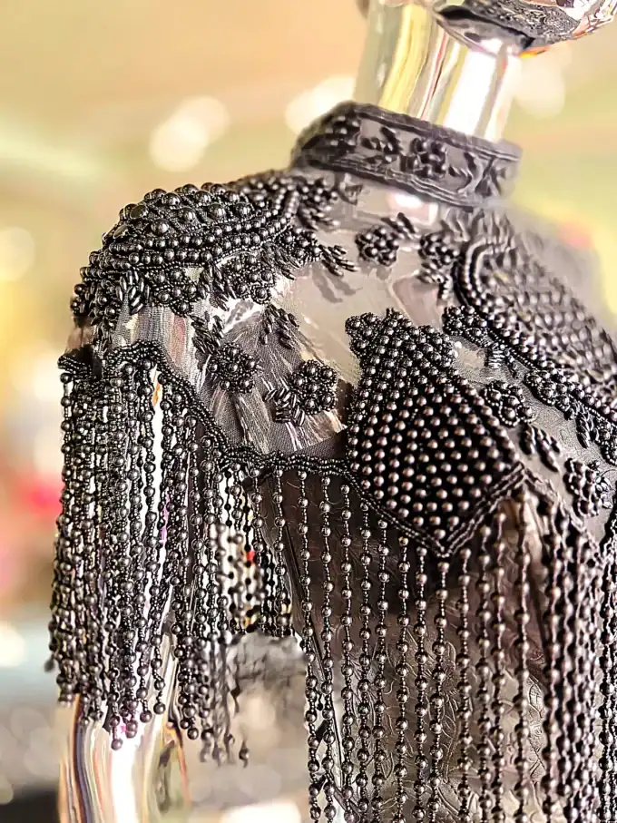 Detaljeret sølvperlekappe med frynser og broderi.