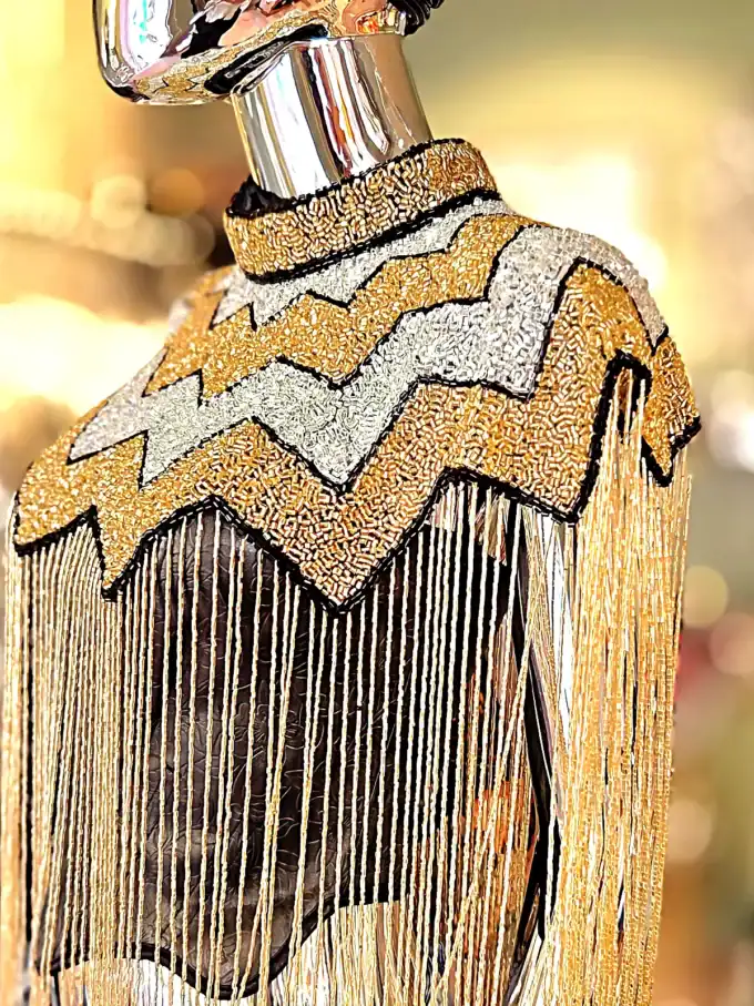 Elegant perlekappe med sort og guld perler, frynser og zigzag mønster.
