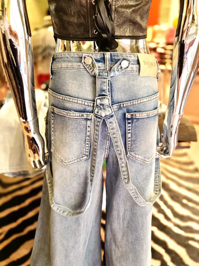 Bred denim bukser med seler på mannequin i butik.