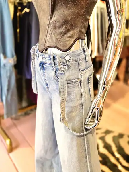 Bred denim bukser med seler og sort top på mannequin.