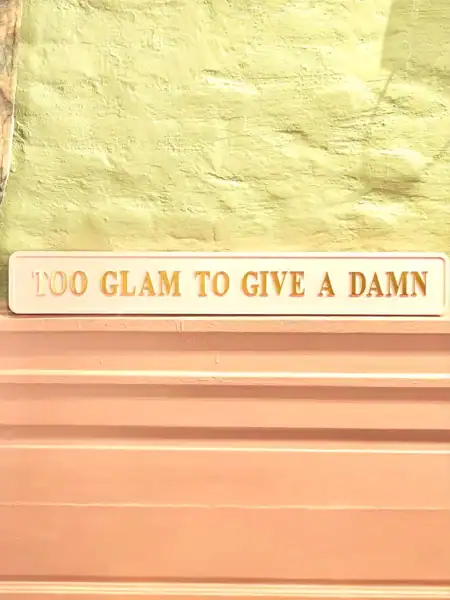 Vægdekoration med citatet '100 GLAM TO GIVE A DAMN' i pastelfarver.