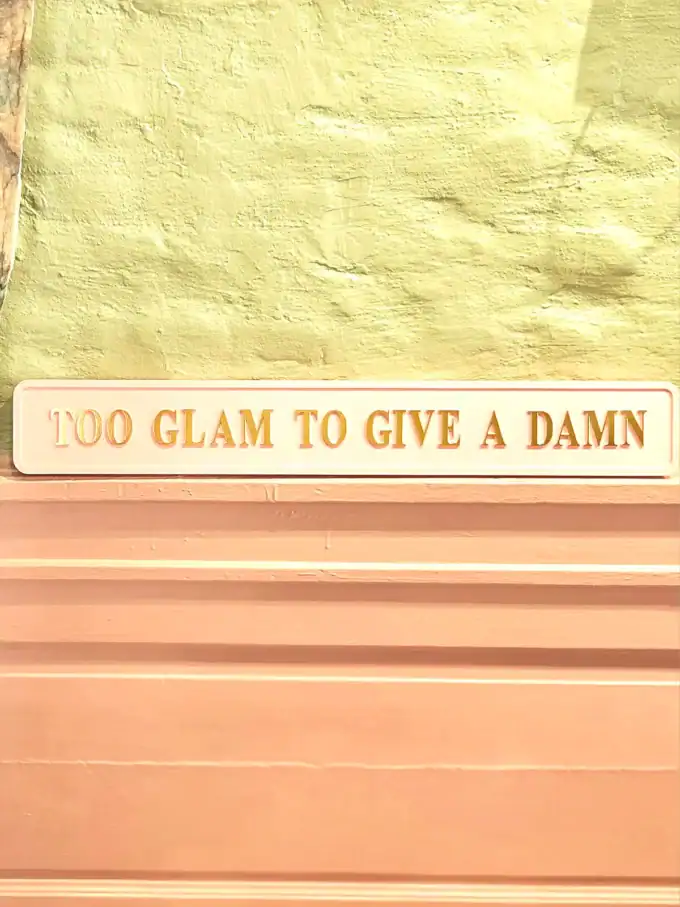 Vægdekoration med citatet '100 GLAM TO GIVE A DAMN' i pastelfarver.