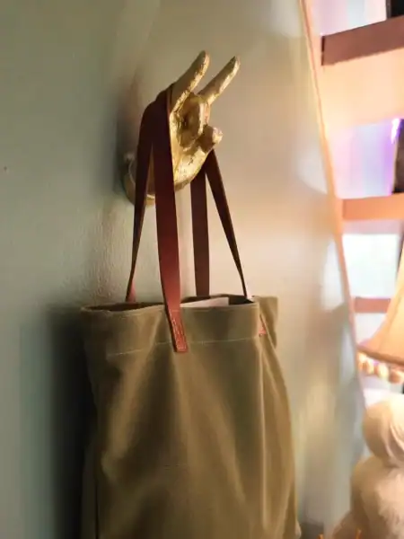Vægkrog med håndformet hånd og taske i beige farve.