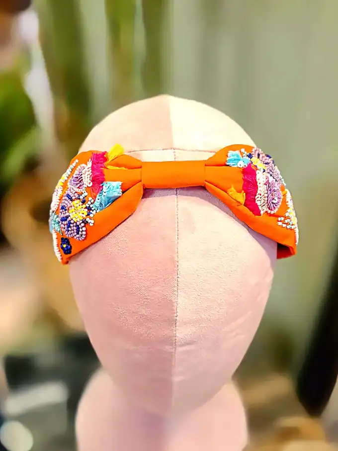 Håndlavet hårbøjle i peach med guldperleblomster og farverige detaljer.