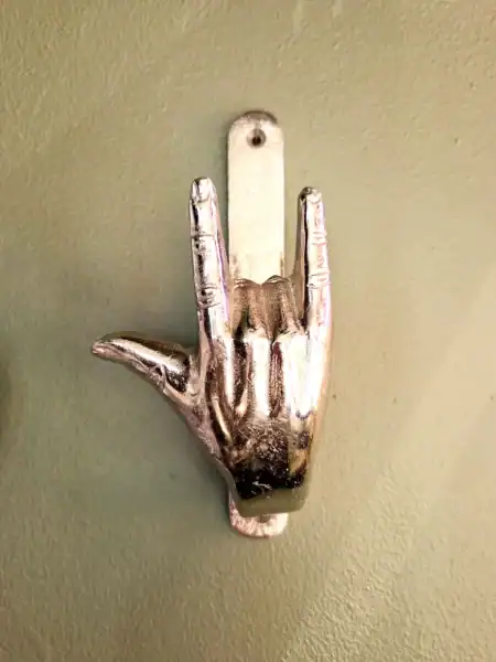 Metal dørhammer i form af hånd, der laver rocktegn, på grøn væg.