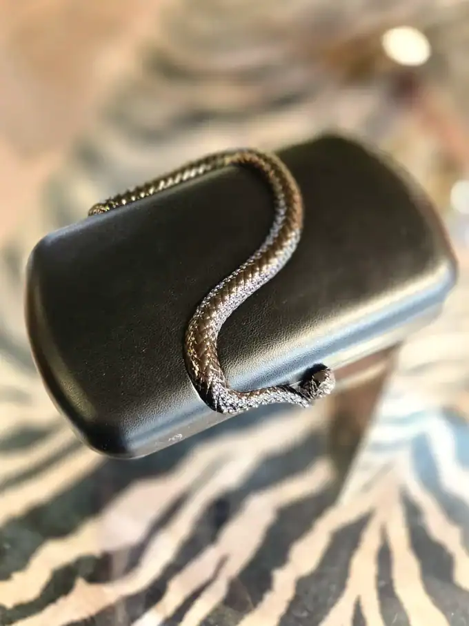 Sort slange clutch med glat overflade og elegant design.