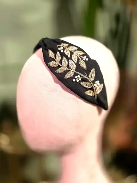 Sort hårbøjle med guld- og perleblomster, perfekt til elegante looks.