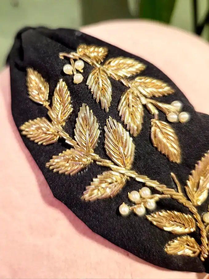 Sort hårbøjle med guld- og perleblomster, perfekt til elegante looks.