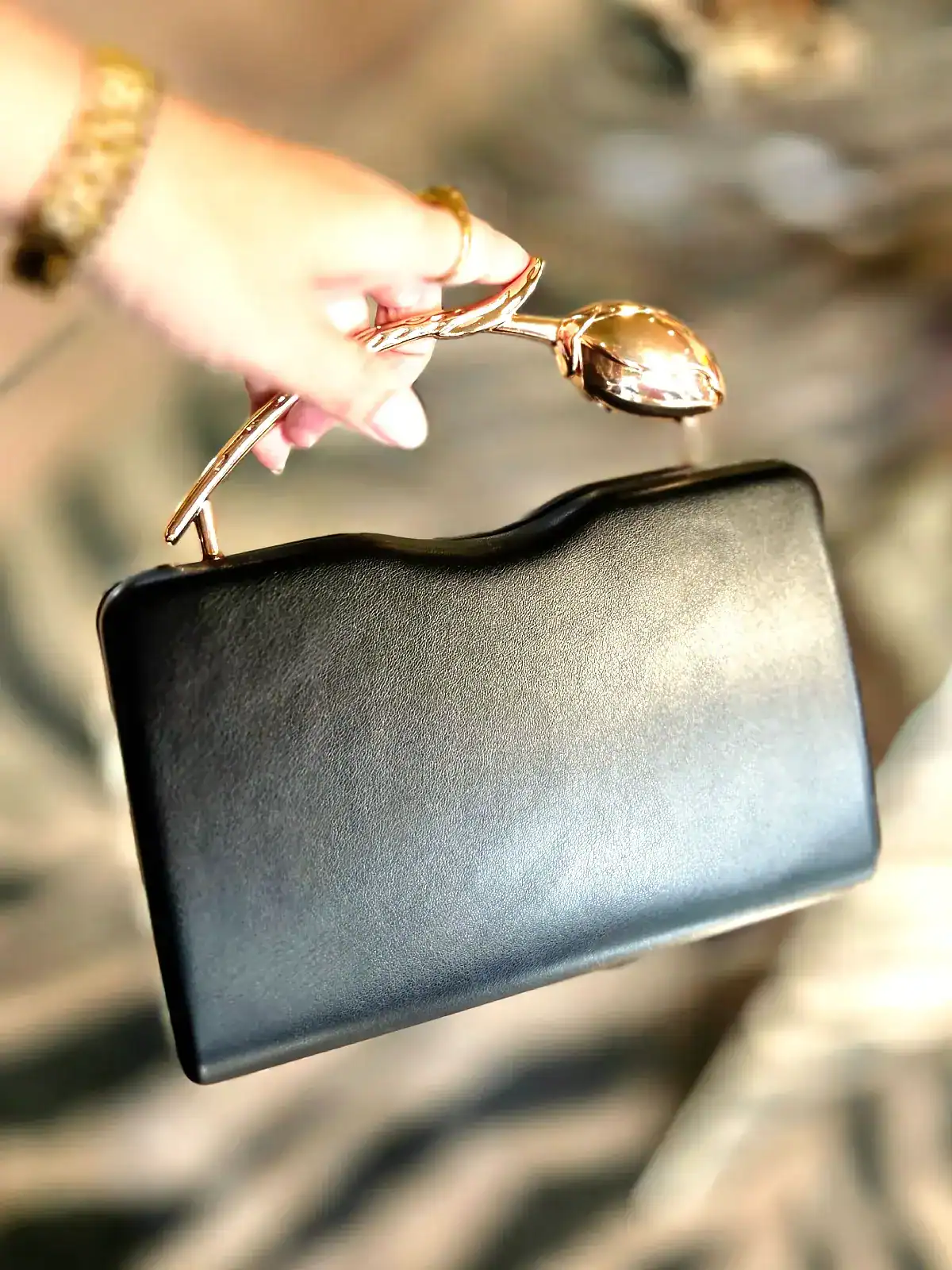 Sort slange clutch med håndtag og gulddetaljer.
