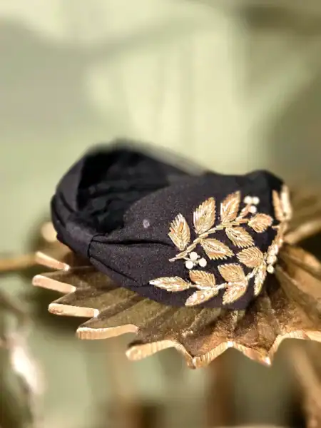 Sort hårbøjle med guld- og perleblomster til elegant styling.