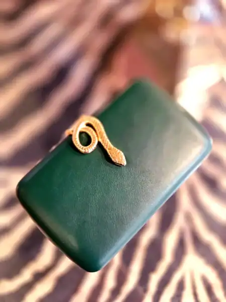 Elegant beige clutch med slange-udskæring og guldfarvet detalje.