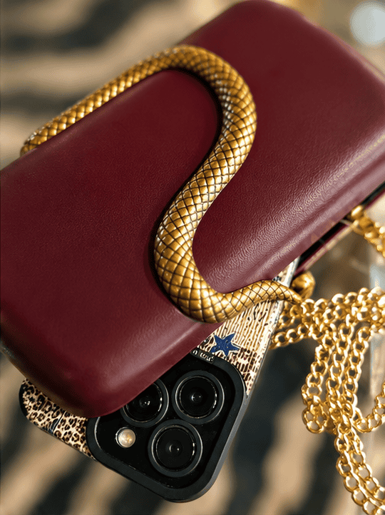 Sort clutch med guldslange og smartphone med leopardmønster.