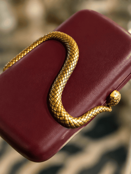 Sort slange clutch med gulddetaljer til elegant brug.