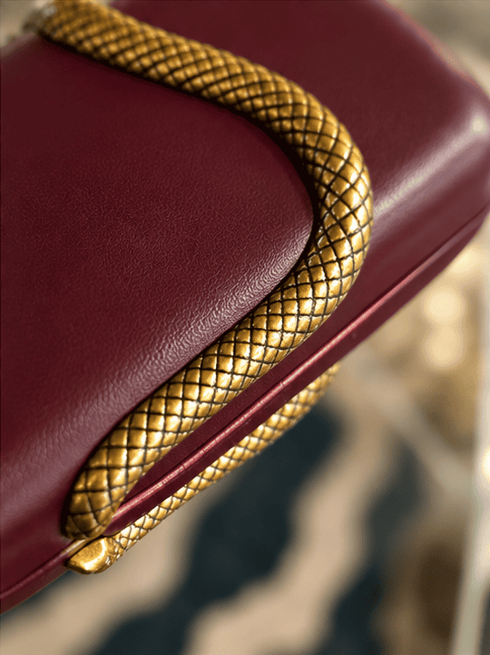 Sort clutch taske med gyldne slangeprintdetaljer.