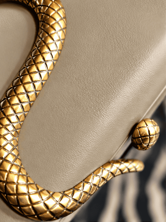 Detalje af slangepræget clutch i khaki med gyldne detaljer.